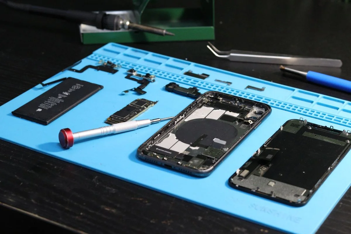 Disassembled mobile phone, battery, screen and precision tools on a blue repair mat